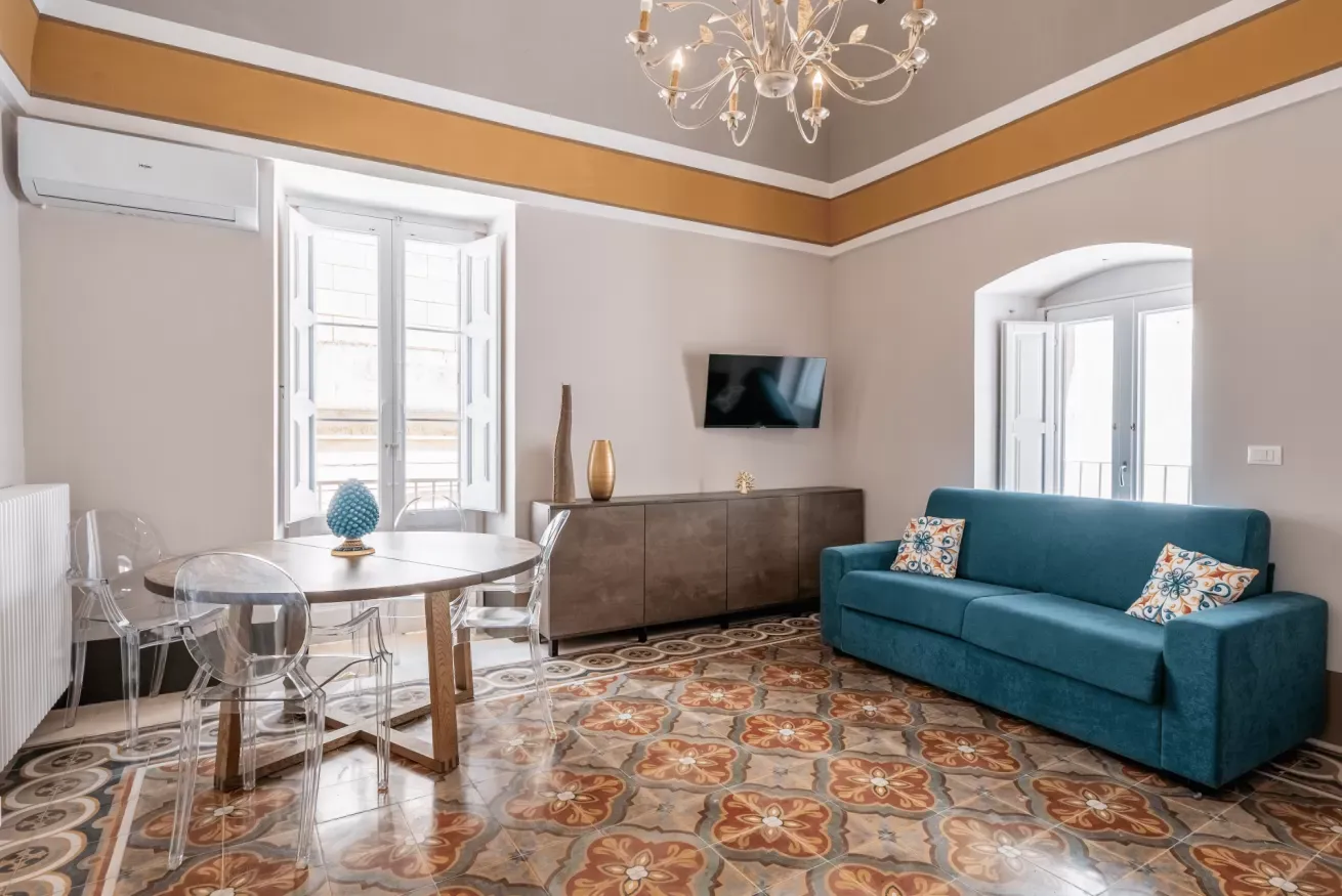 Soggiorno luminoso con tavolo rotondo, divano turchese, TV a parete e pavimento in maiolica decorata