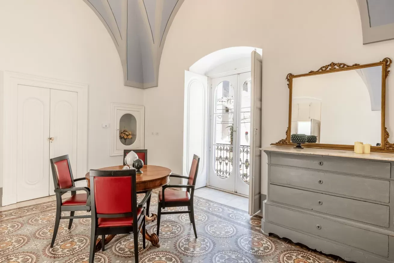 Sala da pranzo elegante con tavolo rotondo, sedie rosse, specchio e porta finestra aperta