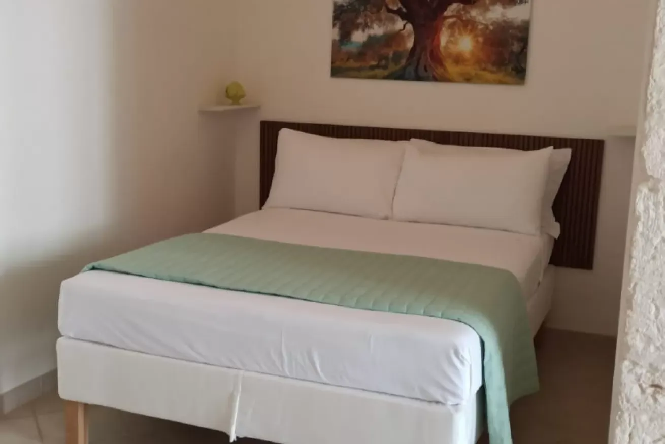 Camera da letto con letto matrimoniale rifatto, coperta verde chiaro e quadro sopra la testiera