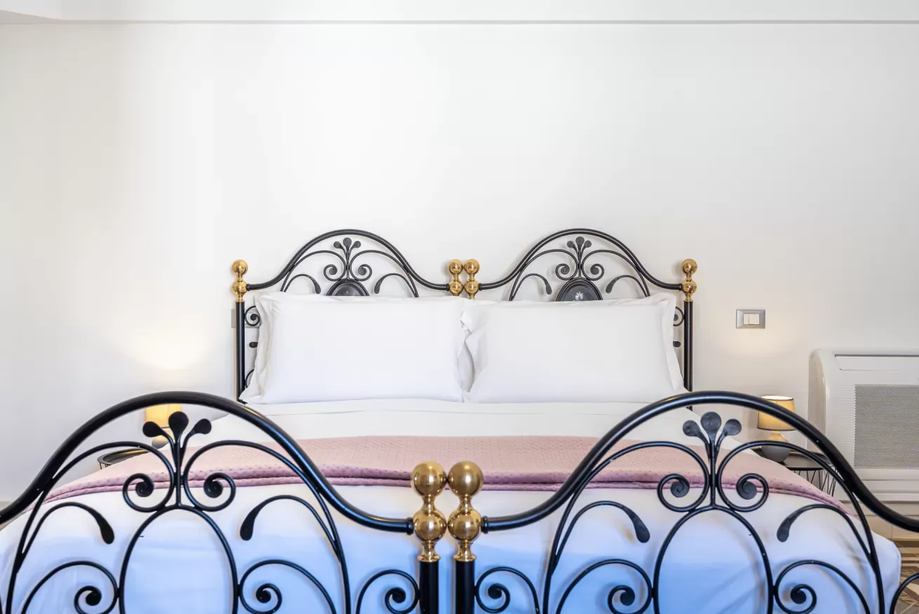 Letto matrimoniale in ferro battuto con biancheria bianca e coperta lilla in una camera luminosa