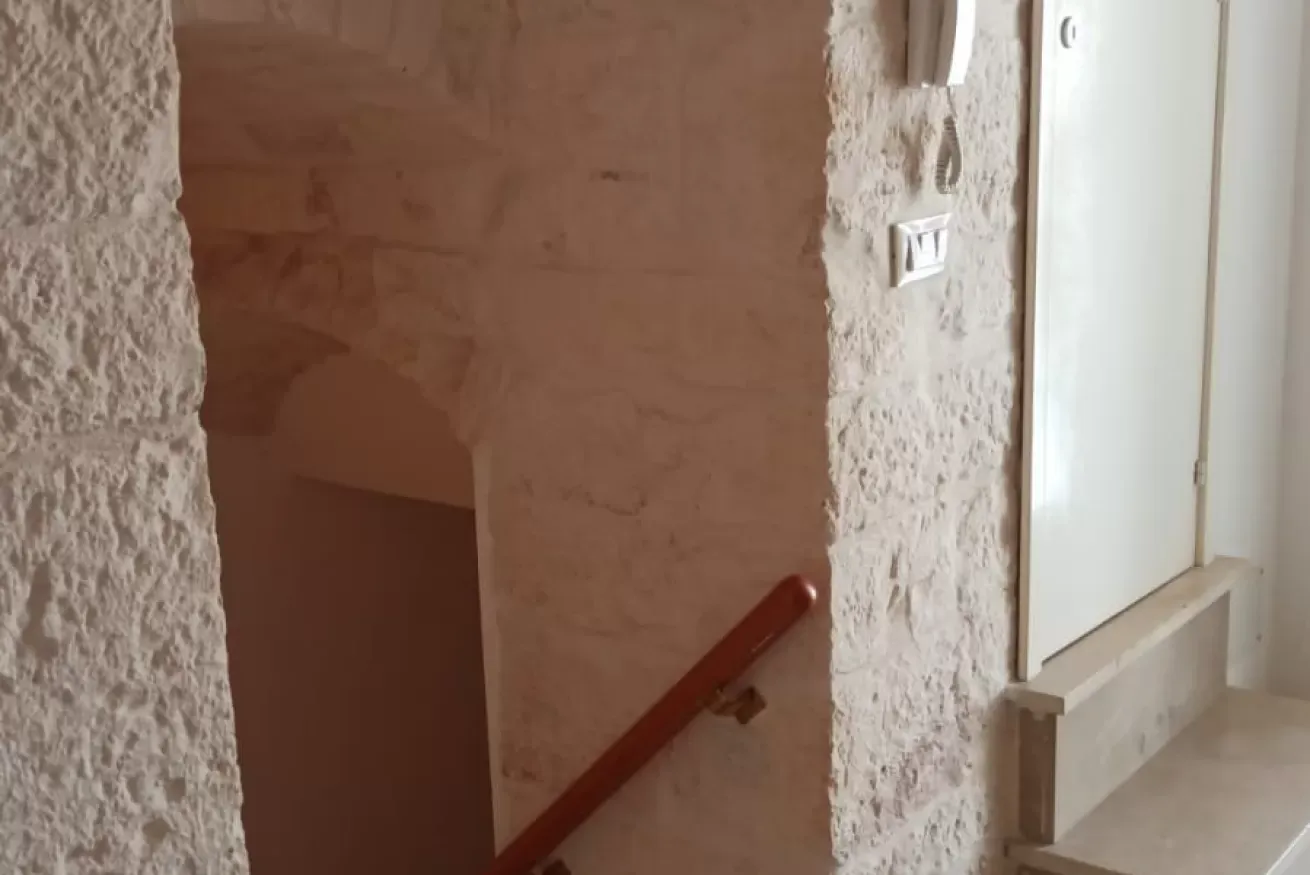 Scala interna in pietra con corrimano rosso e porta bianca a destra