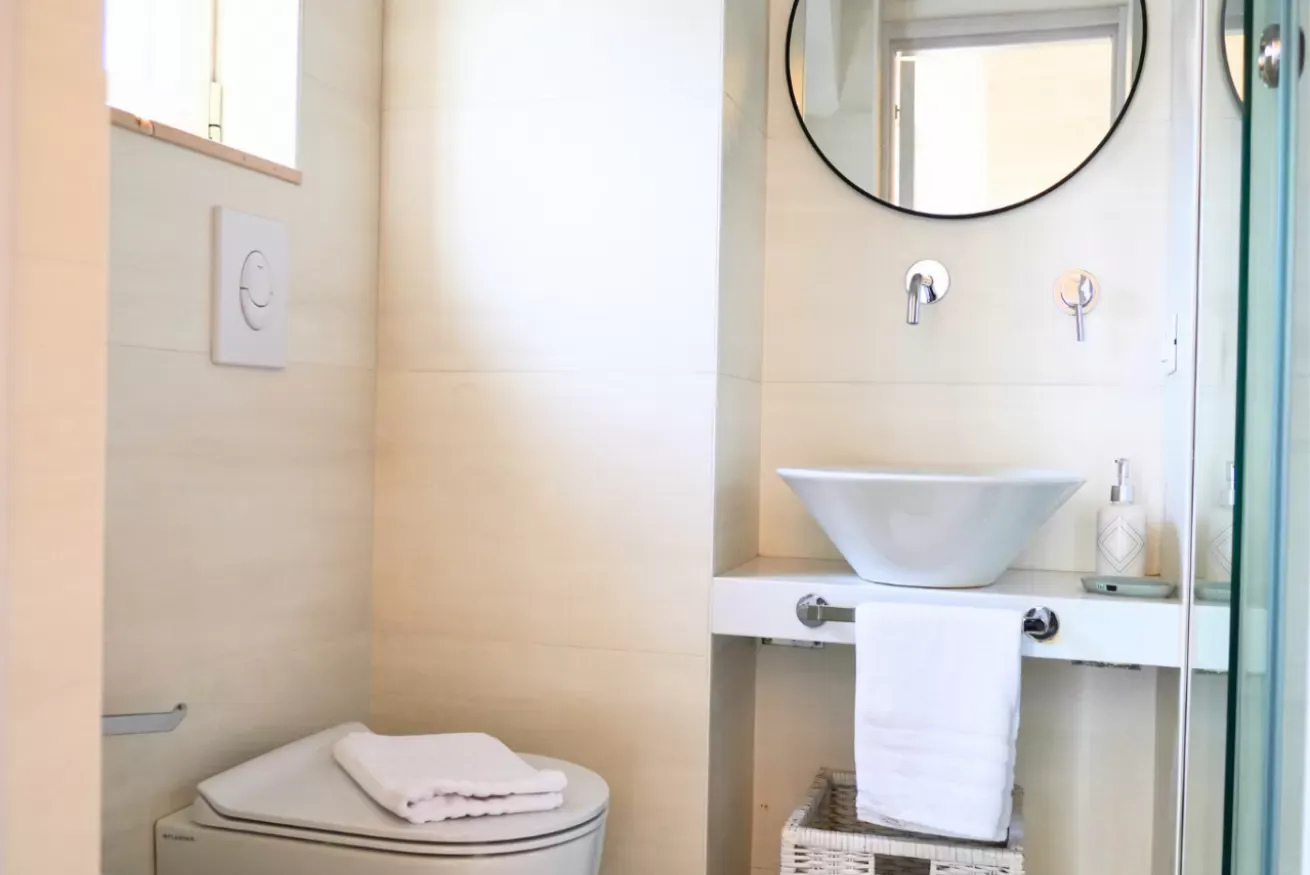 Bagno moderno con lavabo, specchio rotondo, asciugamani e WC