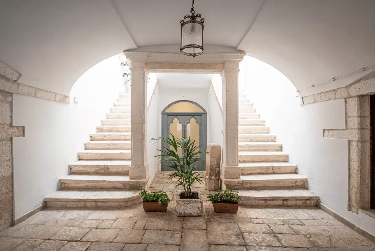 Cortile interno con doppia scala simmetrica, porta centrale e piante in vaso