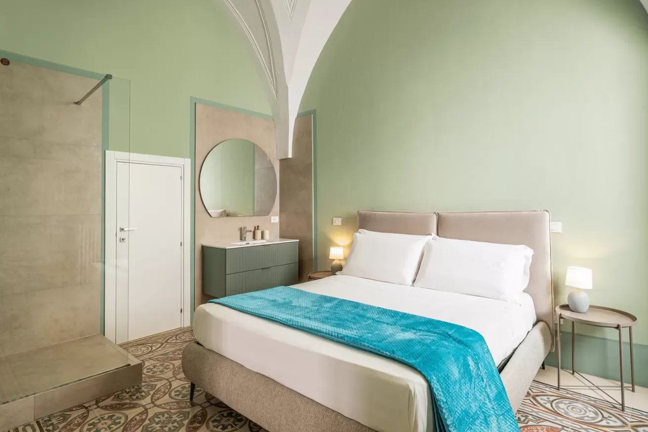 Camera da letto moderna con letto matrimoniale, bagno a vista e pareti verde chiaro