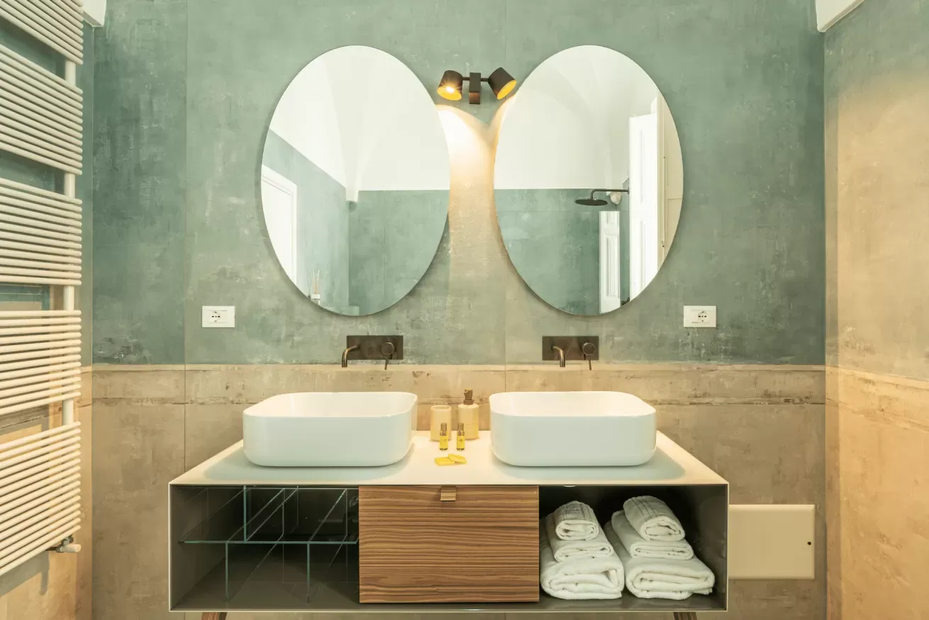 Bagno moderno con doppio lavabo, due specchi ovali e asciugamani piegati sotto il mobile