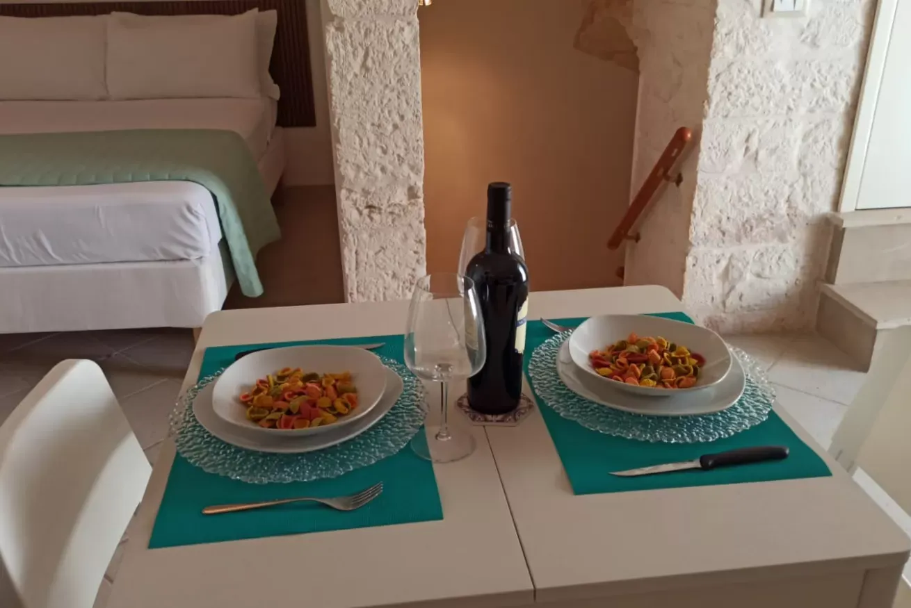 Tavola apparecchiata con due piatti di pasta, bottiglia di vino e bicchieri in una stanza da letto