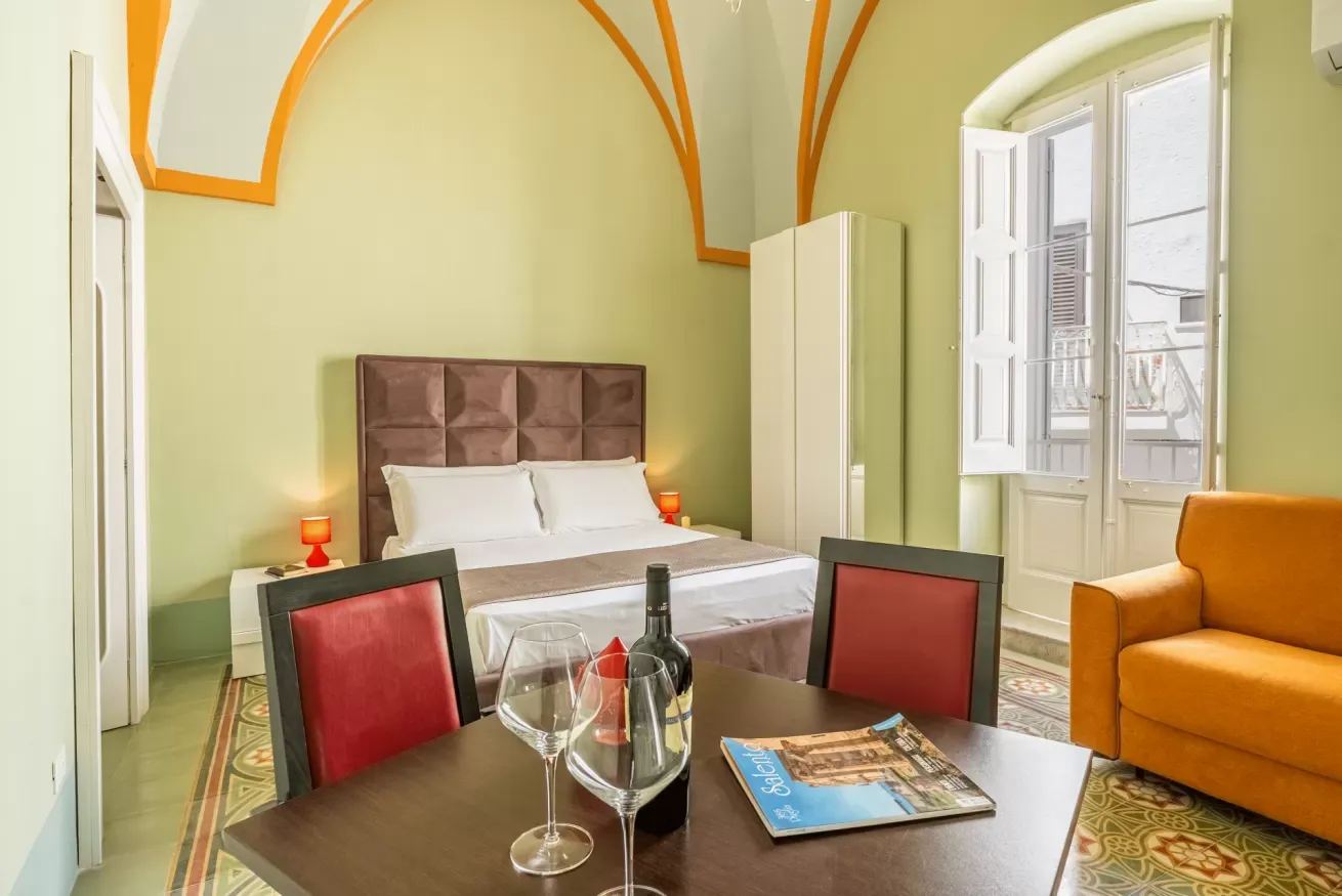 Camera da letto con tavolo apparecchiato, letto matrimoniale, divano arancione e finestra aperta sul balcone